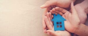 Pair of hands holding a house made out of cardboard